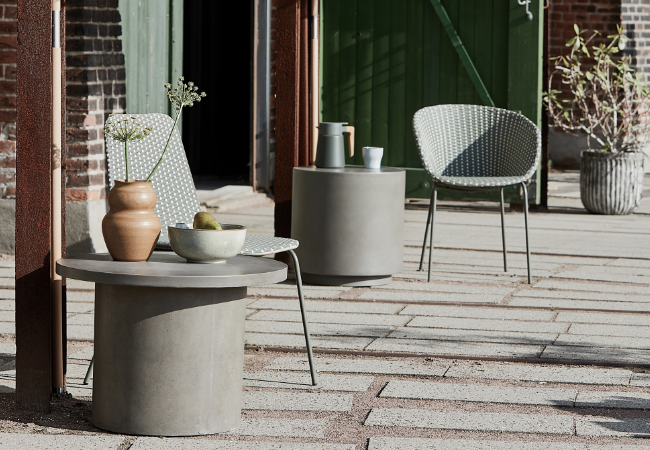 Grå betonborde og lys loungestol i solrigt udendørsmiljø